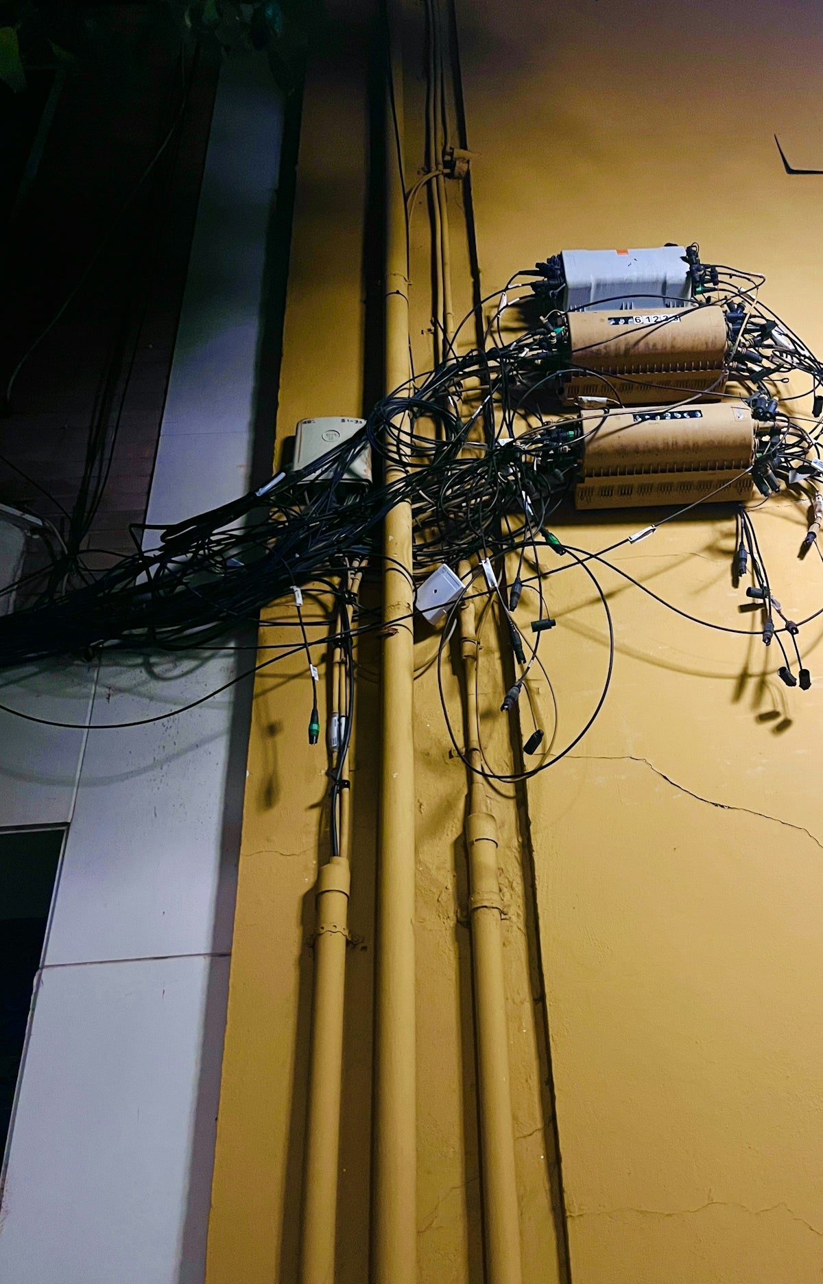 Tangled wires and conduits on a yellow wall